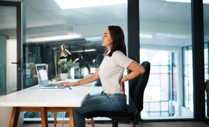 Frau sitzt am Arbeitsplatz mit Rückenschmerzen