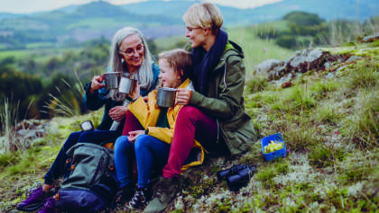 small girl with mother and grandmother sitting and drinking hot tea on top of mountain.