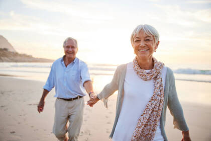 laughing senior woman holding hands with her husband on a beach at sunset