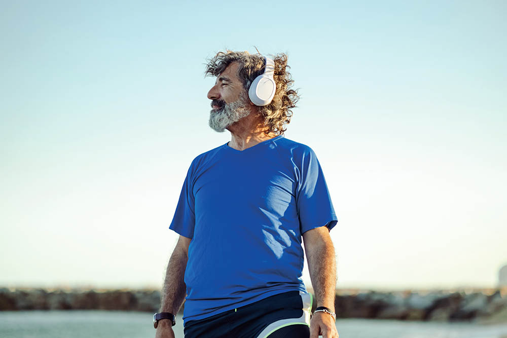 portrait of a good looking senior man enjoying on the beach and listening to music